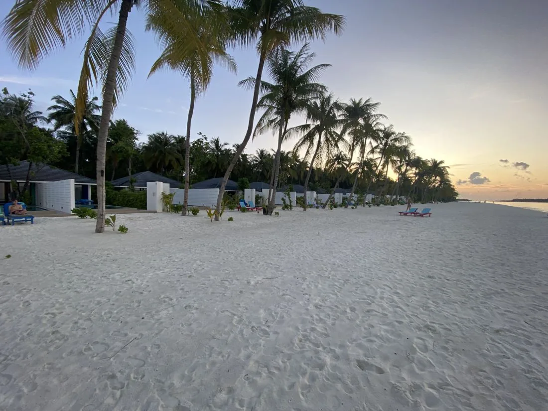 Strand met ligbedden en villa's bij zonsondergang op Sun Island