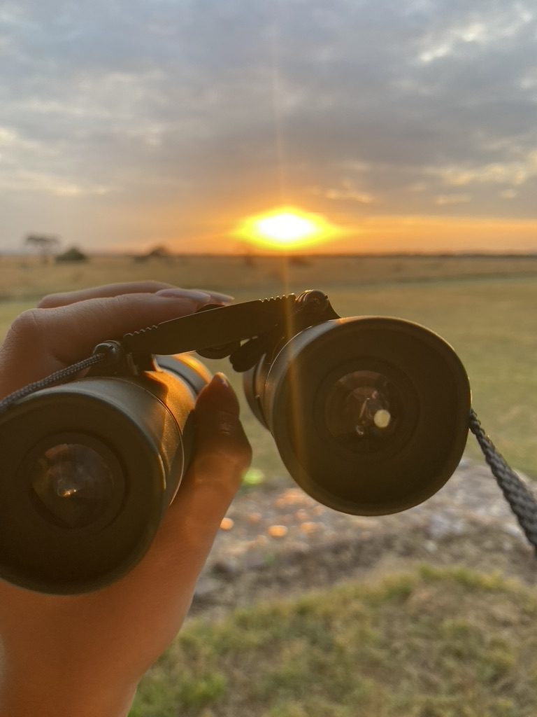 Verrekijker omhoog gehouden tegen de ondergaande zon boven de Serengeti