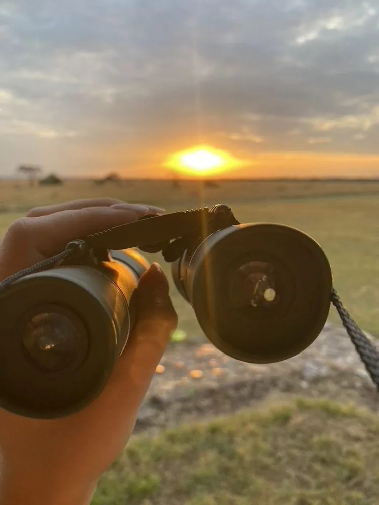Verrekijker omhoog gehouden tegen de ondergaande zon boven de Serengeti